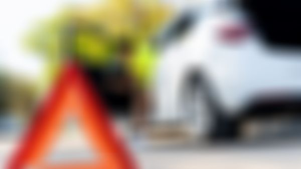 Warndreieck im Vordergrund, Frau steigt im Hintergrund aus weißem Auto aus