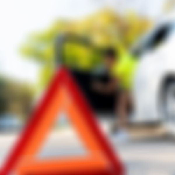 Warndreieck im Vordergrund, Frau steigt im Hintergrund aus weißem Auto aus