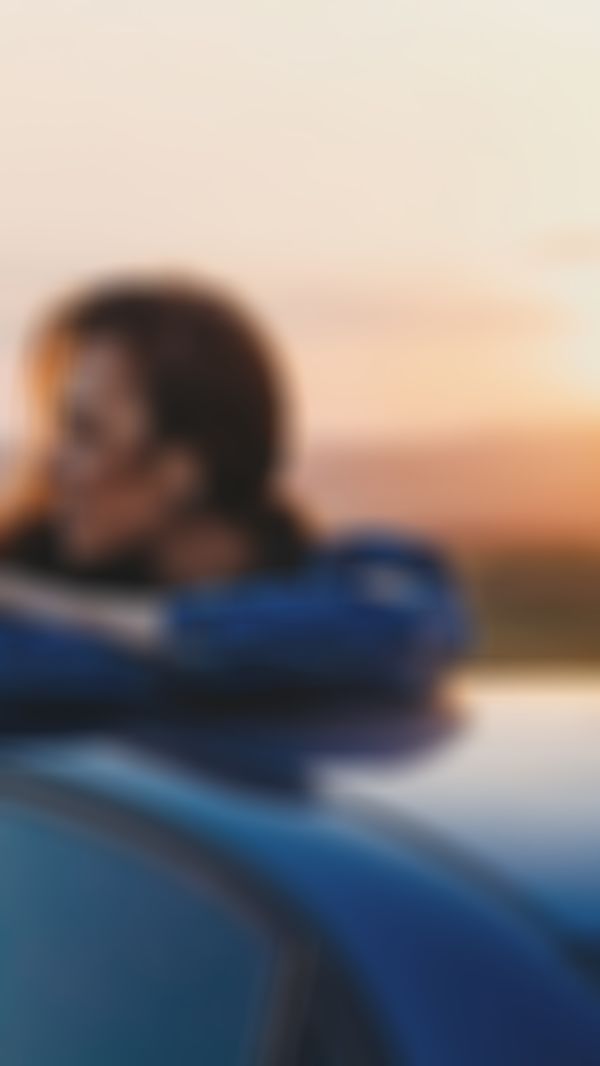 GARANTA Image Sujet - Campende Frau sitzt auf ihrem Autodach und betrachtet das Bergpanorama