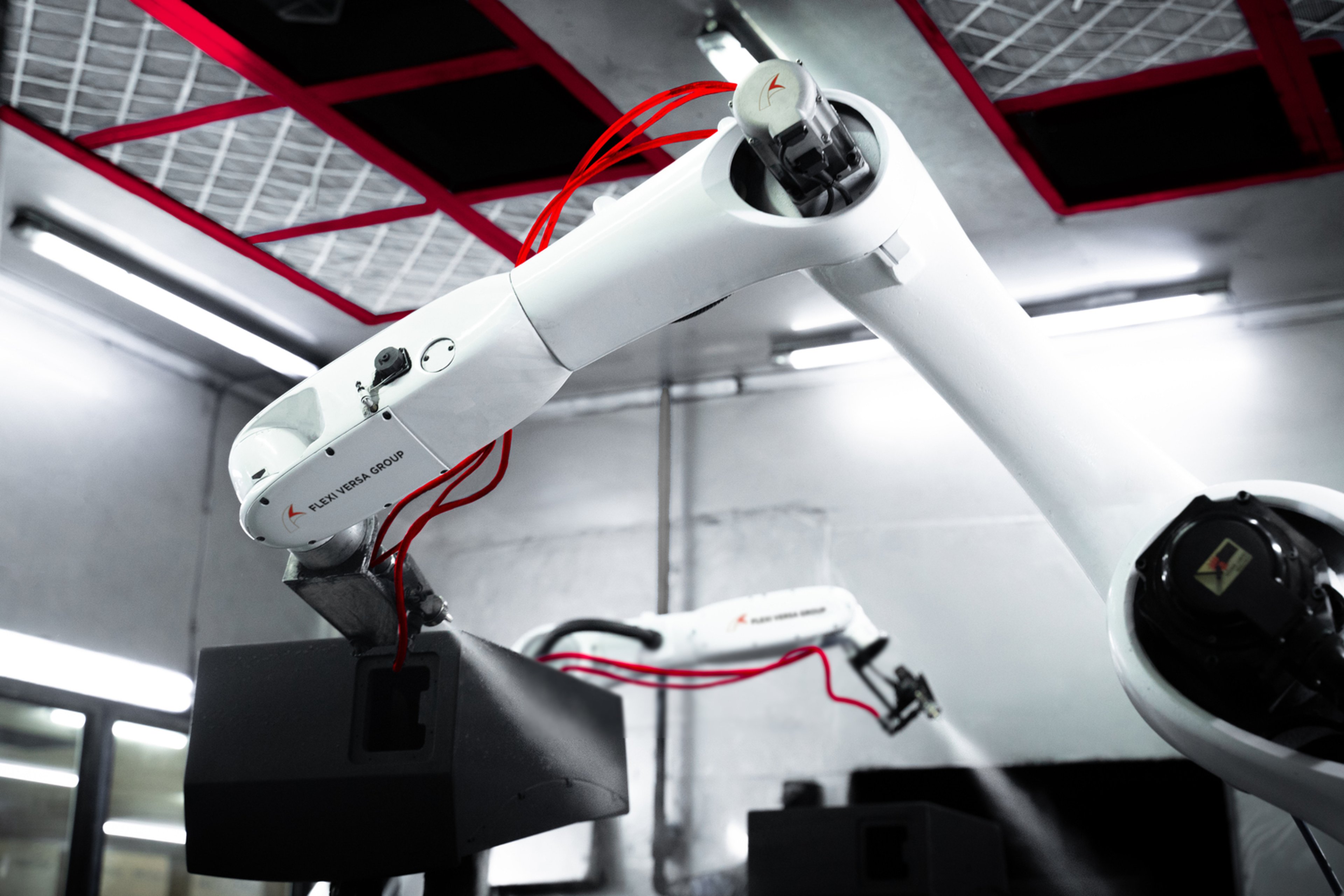 Robotic arms equipped with spray painting tools and red cables operating in a modern industrial environment.