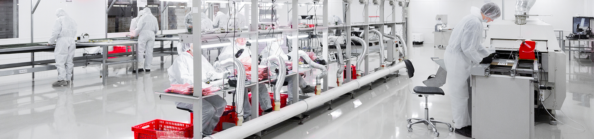 Workers in Cleanroom Suits Operating Machinery in Manufacturing Facility Workers in cleanroom suits operate machinery and assemble products in a sterile, high-tech manufacturing facility with bright lighting.