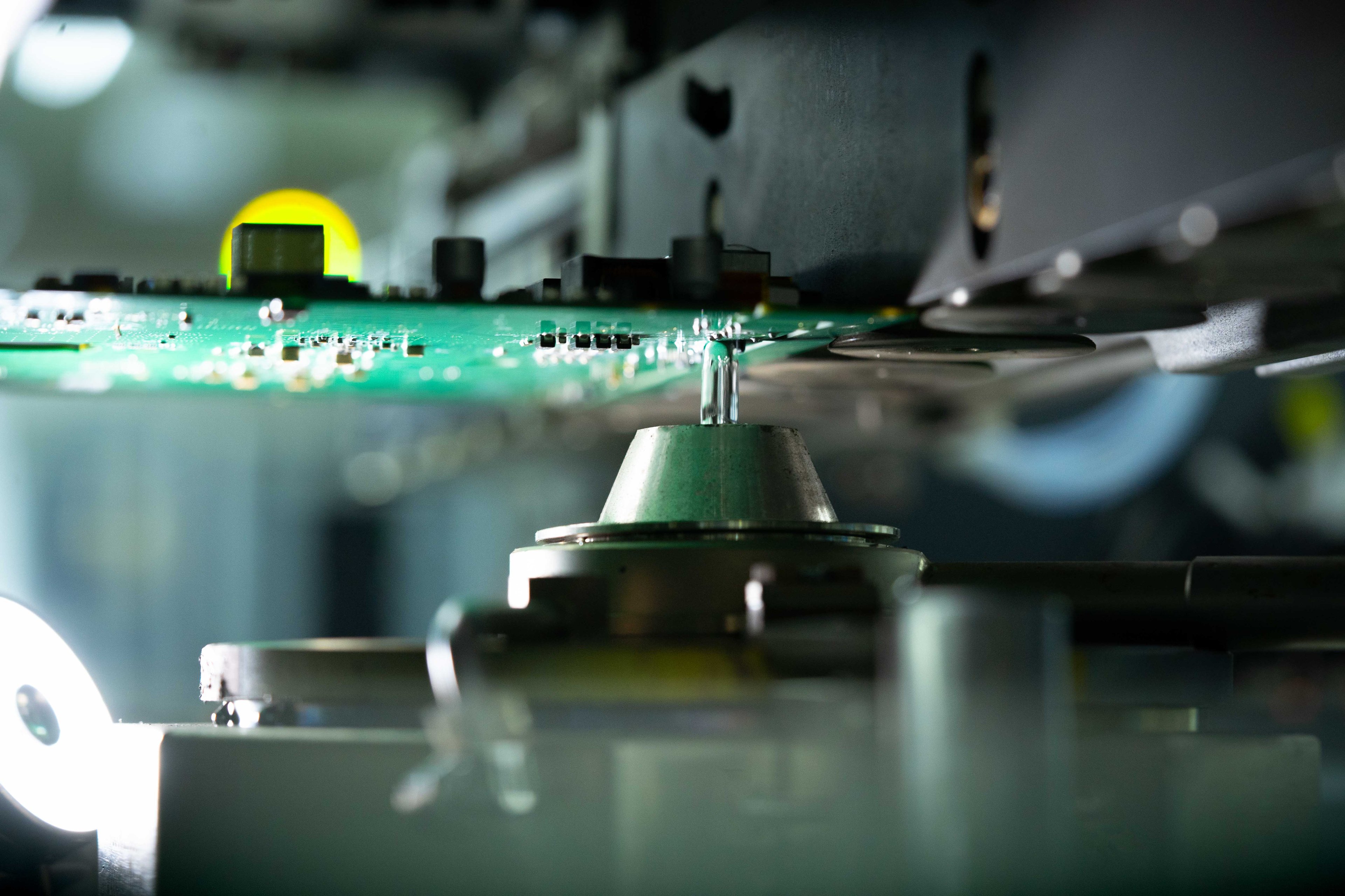 Close-up of a circuit board with electronic components being assembled by a machine in a factory setting.