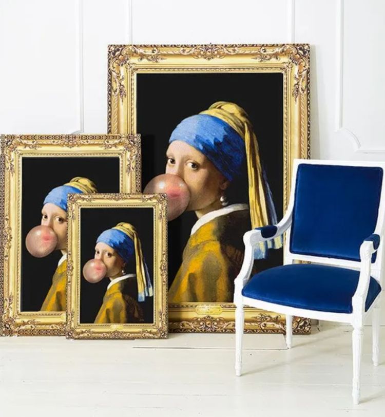 Three framed prints of a classic painting with a modern twist, featuring a girl blowing bubblegum, beside a blue velvet chair.