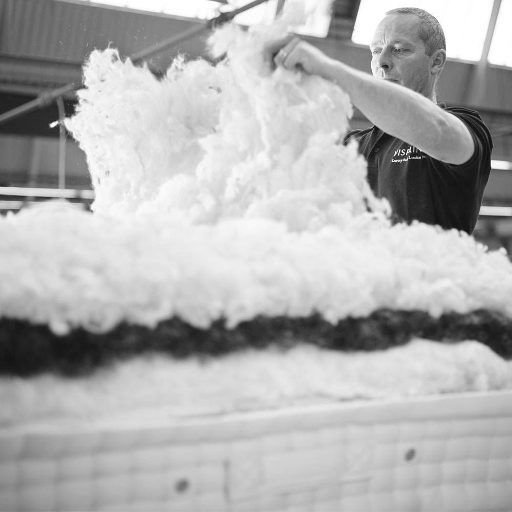 A person arranging fluffy white material inside a factory setting, with a focus on texture and layers. Black and white image.