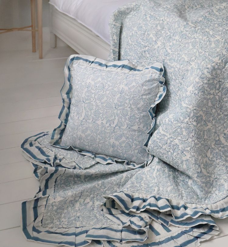 Floral-patterned pillow and blanket with blue and white stripes on the floor near a bed, creating a cozy and elegant atmosphere.
