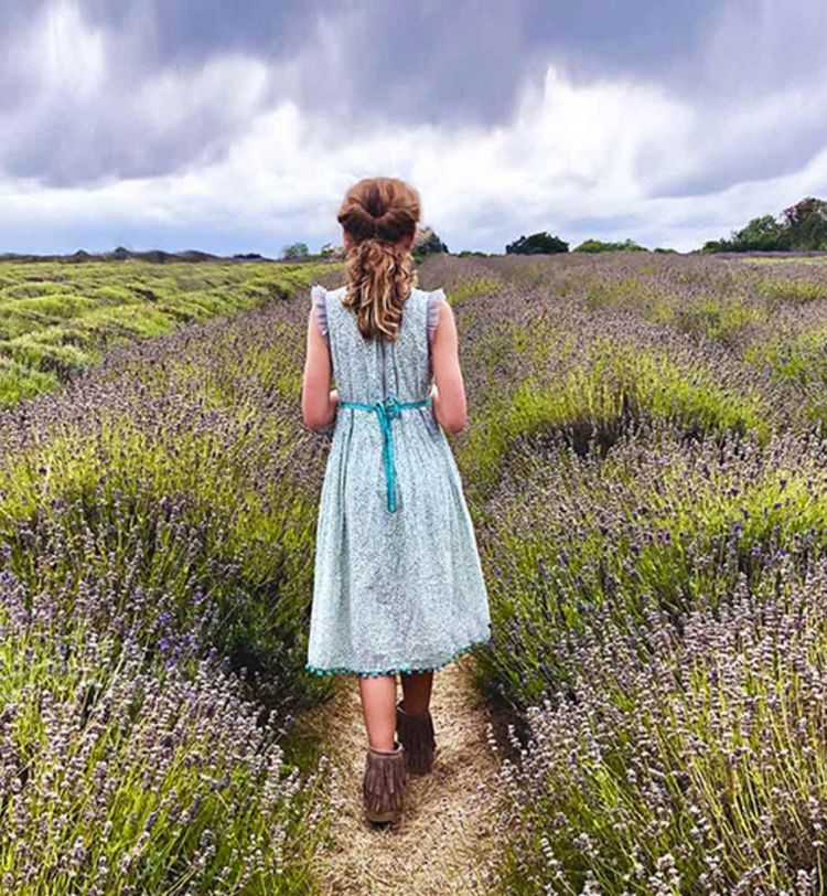 Girl in a light dress walks through a lavender field under a cloudy sky.