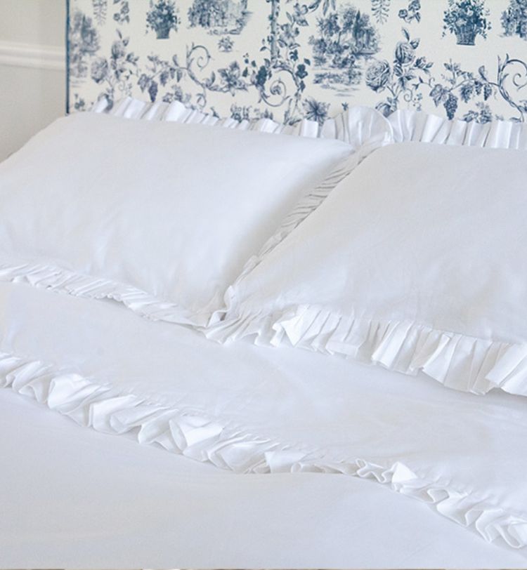 White bed with ruffled pillows and sheets, set against a blue and white patterned headboard.