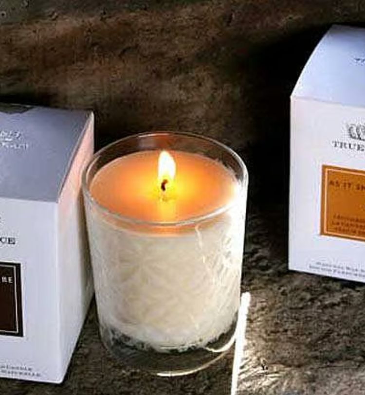 A lit candle in a glass holder is placed between two boxed candles on a rustic wooden surface.