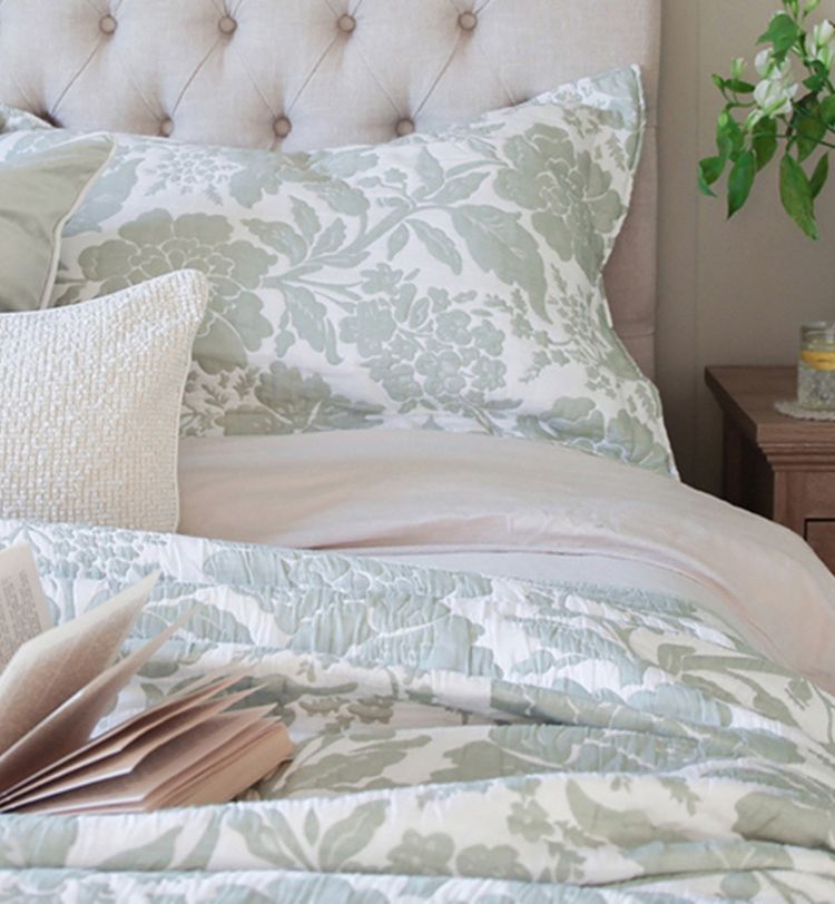 Cozy bed with floral-patterned pillows and comforter, open book, and a wooden nightstand with a plant and candle.
