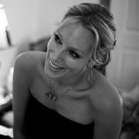 Smiling woman with long hair and hoop earrings in a strapless top, captured in a candid, black and white photo indoors.