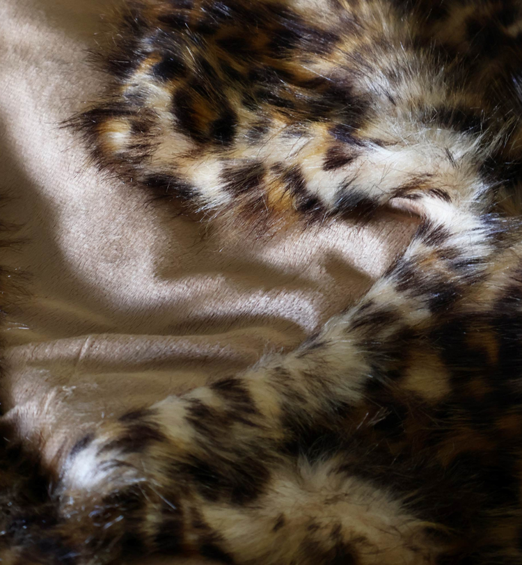 Close-up of a leopard print faux fur fabric with a soft beige lining, showing texture and pattern detail.