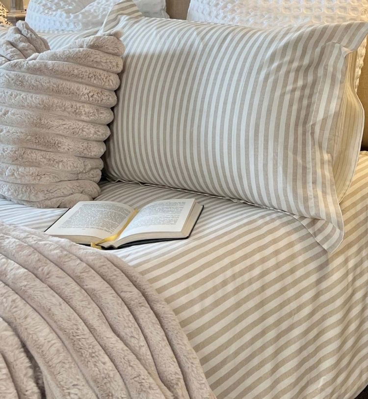 A cozy bed with striped pillows and blanket, a textured cushion, and an open book resting on the neatly arranged bedding.