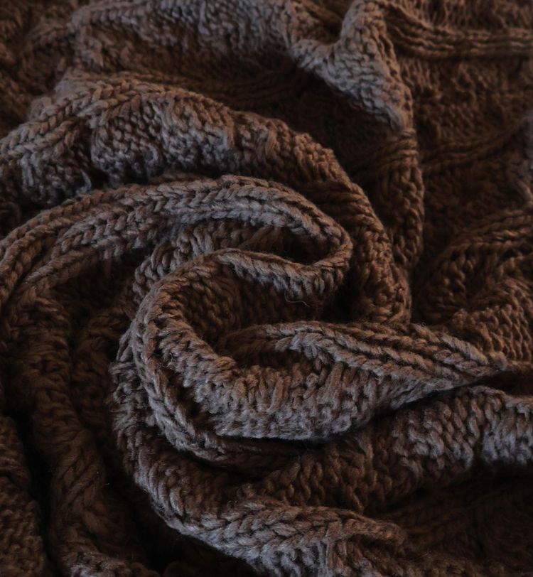 Close-up of a textured, dark brown knitted fabric with intricate patterns, creating a cozy and warm appearance.