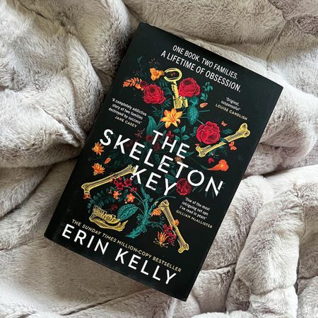 Book titled "The Skeleton Key" by Erin Kelly on a fluffy, light-colored blanket. Cover features flowers and golden keys.