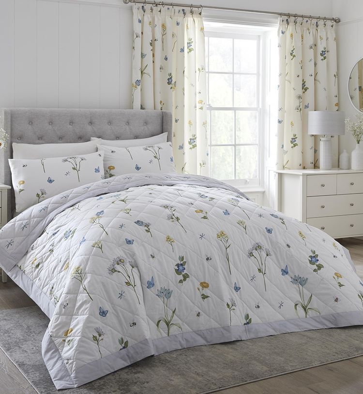 Bedroom with floral bedding, matching curtains, and a tufted headboard. Light-filled window, white furniture, and decorative flowers enhance the decor.