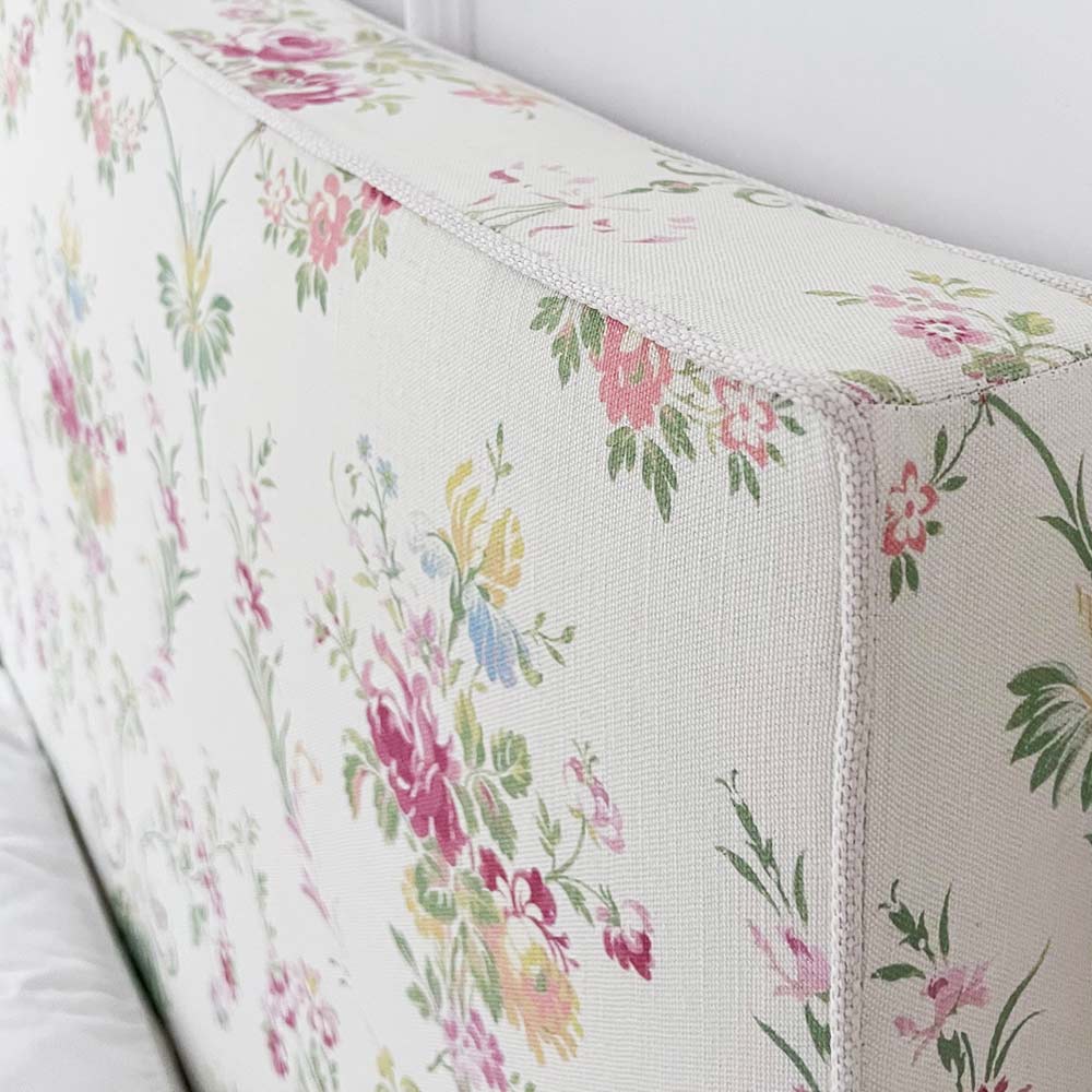 Close-up of a floral-patterned fabric headboard with pink, green, and yellow flowers on a white background.