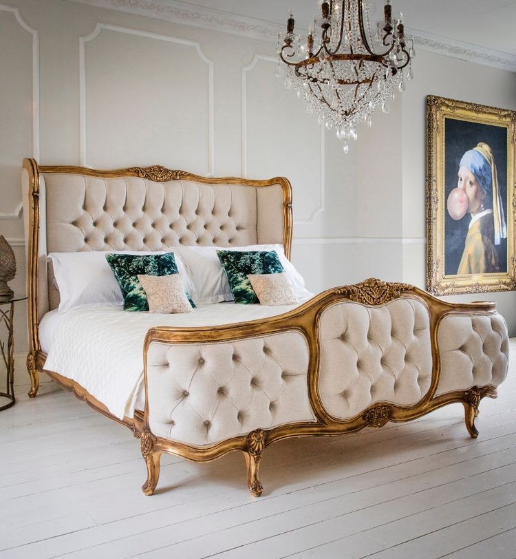 Elegant bedroom with a vintage-style bed, tufted headboard and footboard, ornate chandelier, and a painting on the wall.