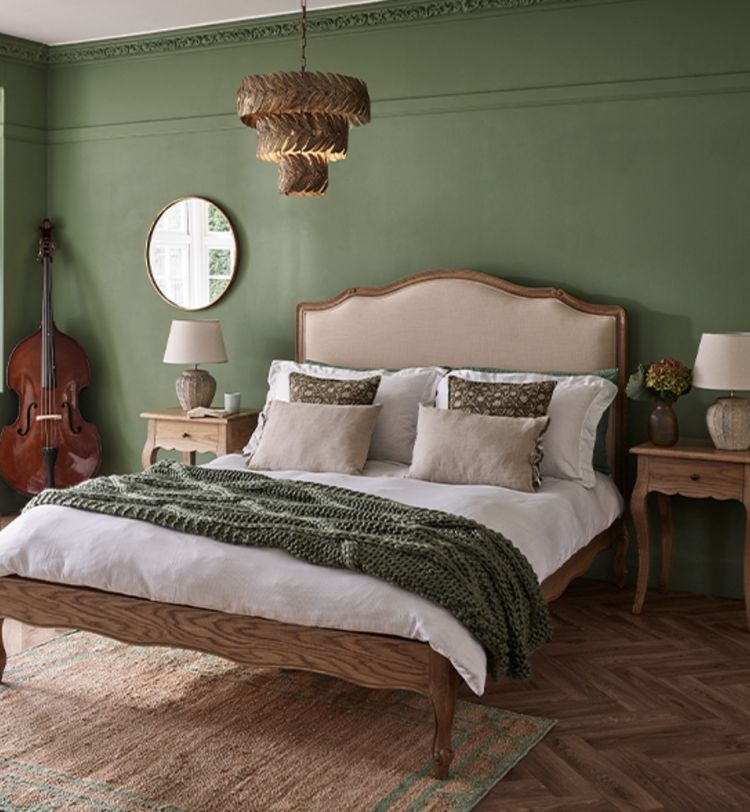 Cozy bedroom with a wooden bed, green walls, and a double bass in the corner. Rustic lamps, side tables, and a woven chandelier add warmth.
