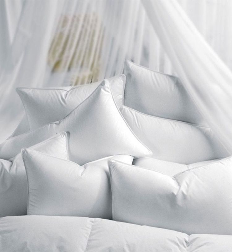 A pile of soft, white pillows arranged on a bed, surrounded by sheer white curtains, creating a cozy and inviting atmosphere.