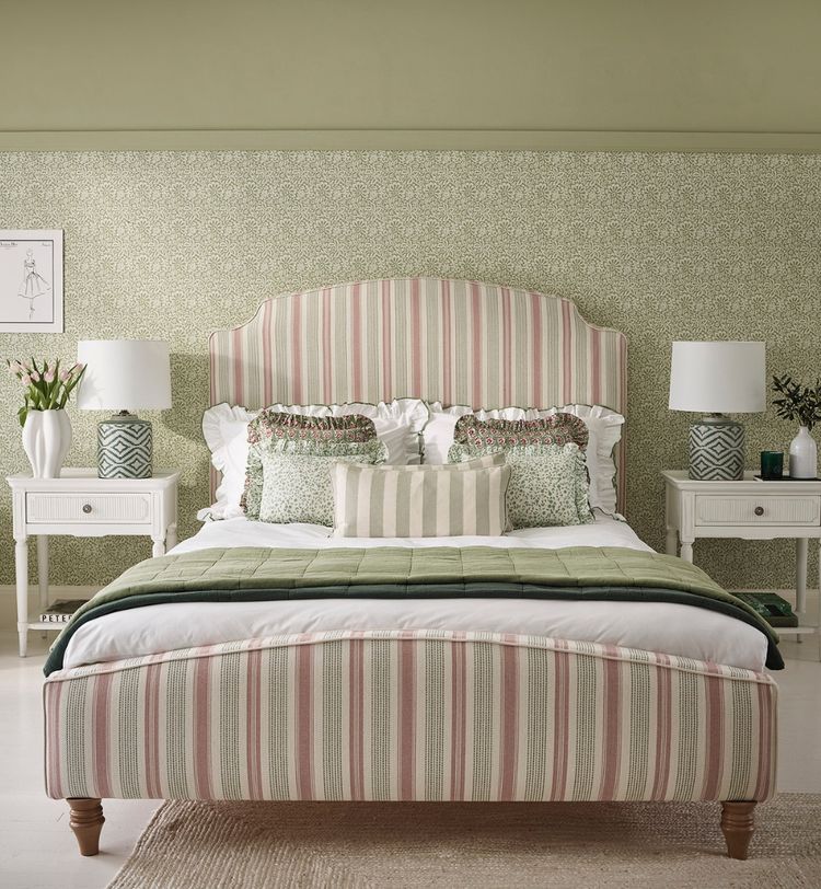 Cozy bedroom with a striped headboard, patterned wallpaper, and green accents. Two nightstands with lamps and floral decor complete the look.
