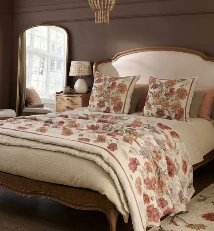 Cozy bedroom with a wooden bed, floral-patterned bedding, matching pillows, a bedside table, and a large window with soft natural light.