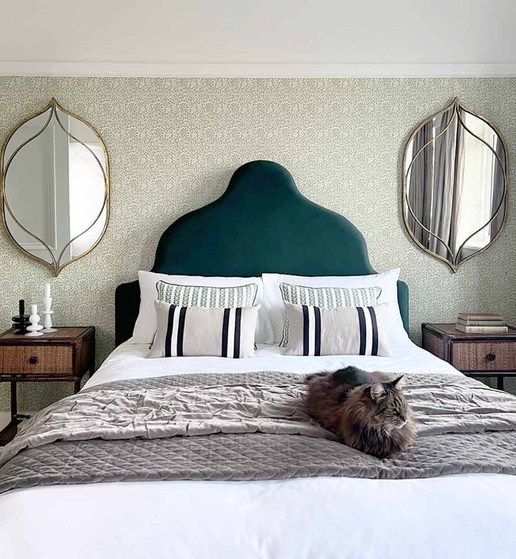 Bedroom with a green headboard, decorative mirrors, and a fluffy cat on the bed. Nightstands with candles and a textured wall complete the look.