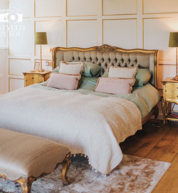 Elegant bedroom with a tufted headboard, two bedside tables with lamps, and a bench at the foot of the bed. Warm lighting and wooden floor.