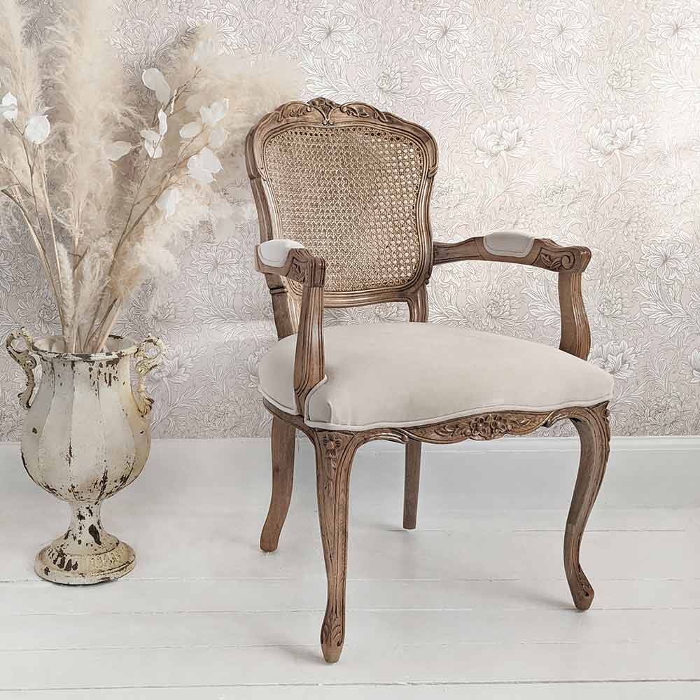 Elegant wooden chair with a woven back and cushioned seat beside a decorative vase with pampas grass, set against a floral wallpaper.