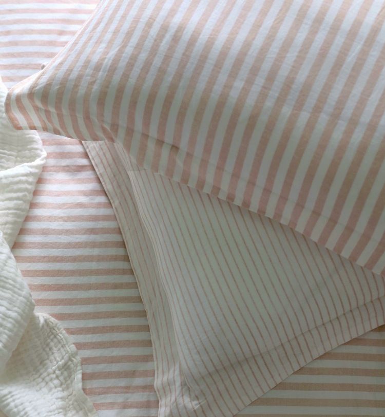 Two pillows with pink and white stripes on a matching bedsheet, next to a textured white blanket.