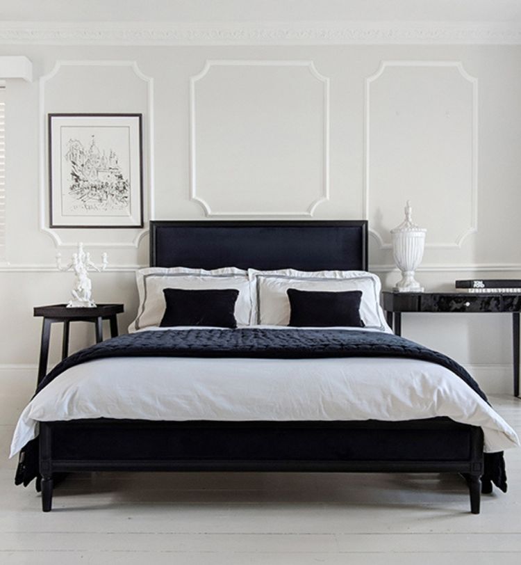 Elegant bedroom with a black bed, white bedding, two side tables, and framed artwork on a white paneled wall. Minimalist decor.