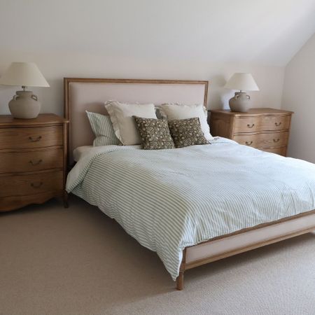 Cozy bedroom with a neatly made bed, striped bedding, decorative pillows, and wooden nightstands with lamps on each side.