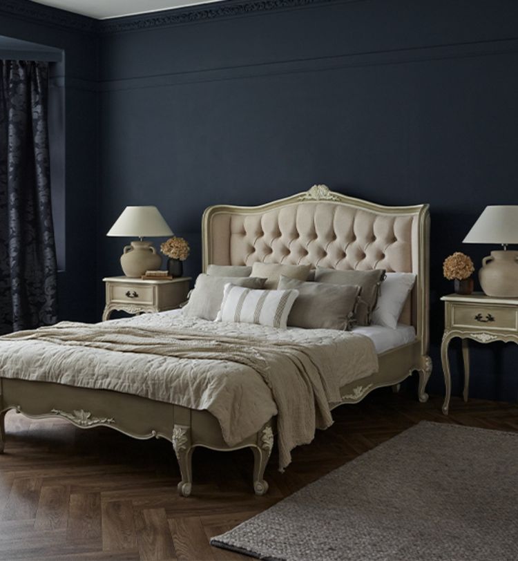 Elegant bedroom with a tufted headboard, beige bedding, and vintage nightstands. Dark walls contrast with light decor, creating a cozy ambiance.