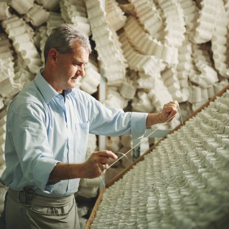 Man in a light blue shirt inspects coiled springs in a workshop, surrounded by stacks of similar springs in the background.