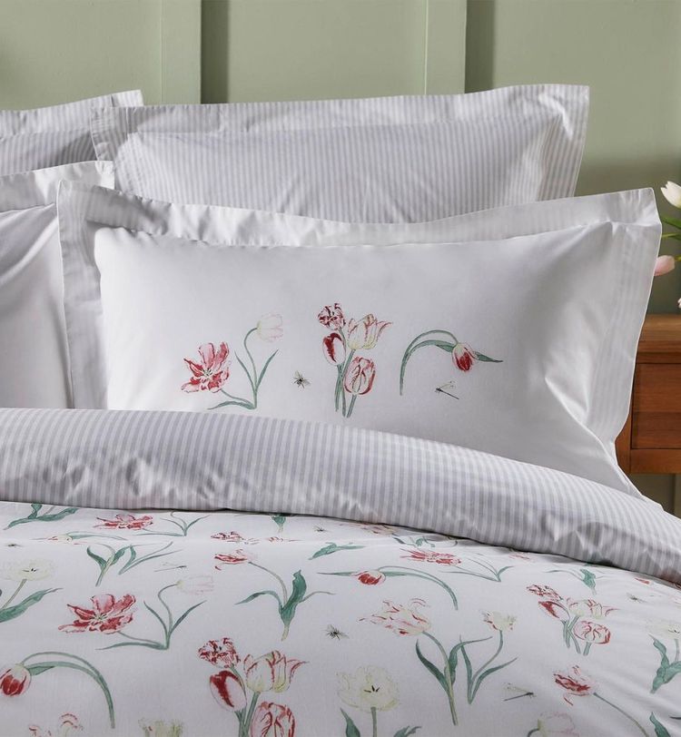 White bedding with floral designs featuring red and pink tulips, set against a light green wall and wooden nightstand.