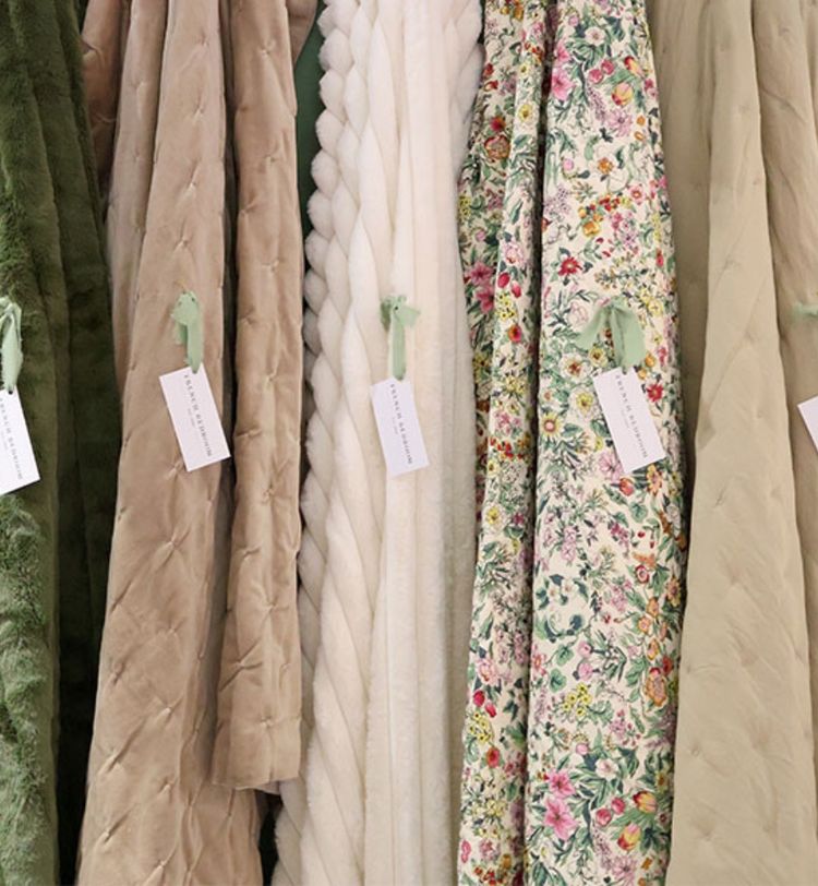 A row of cozy blankets in various textures and colors, including green, beige, white, and floral patterns, displayed with tags.