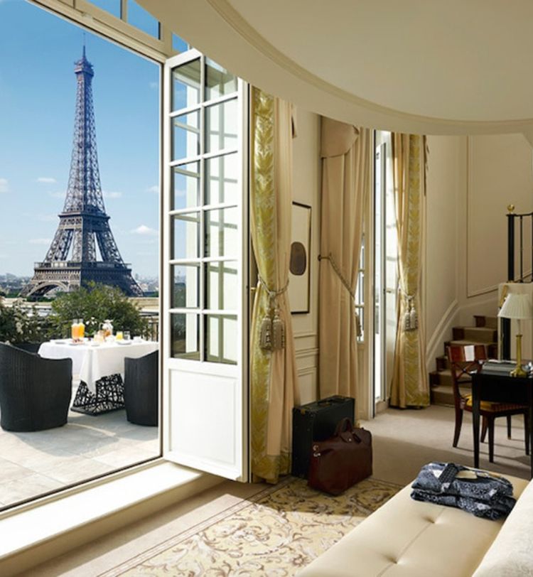 Luxurious hotel room with open French doors leading to a terrace, offering a stunning view of the Eiffel Tower.