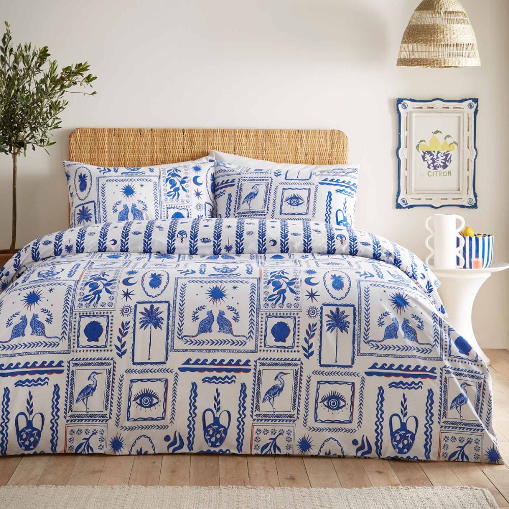 A bed with blue and white patterned bedding featuring nature motifs, a wicker headboard, and a side table with a framed artwork and decor.