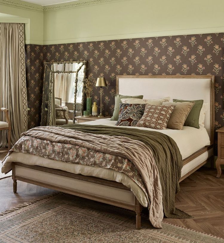 Cozy bedroom with a large bed, patterned pillows, floral wallpaper, green walls, a mirror, and a window with curtains.