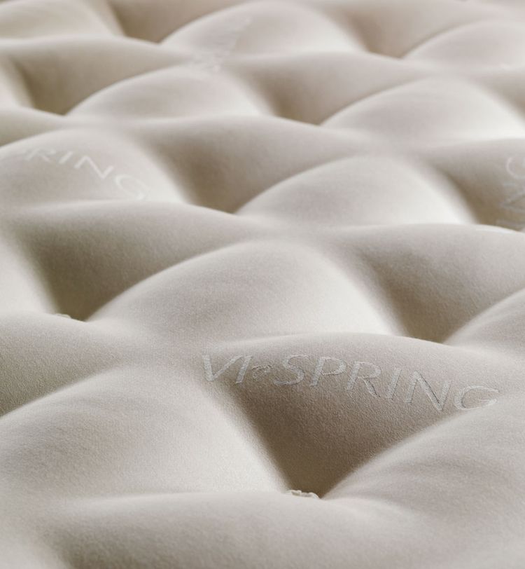 Close-up of a plush, beige mattress surface with embossed "Vi-Spring" logos, featuring a quilted, tufted pattern for added texture.