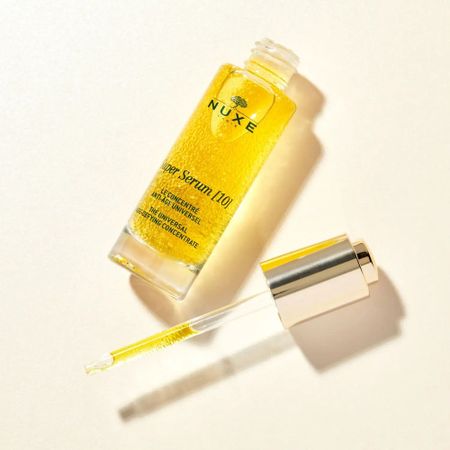 A bottle of Nuxe Super Serum [10] with a dropper, filled with golden liquid, on a light background.