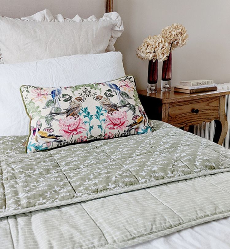 Bed with a floral quilt and pillow, wooden nightstand with dried flowers in vases, and a small stack of books.