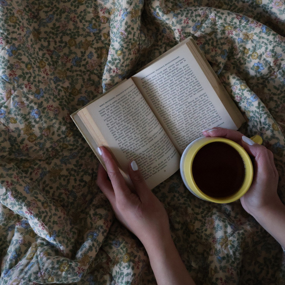 Book and a coffee in bed with a floral quilted bedspread