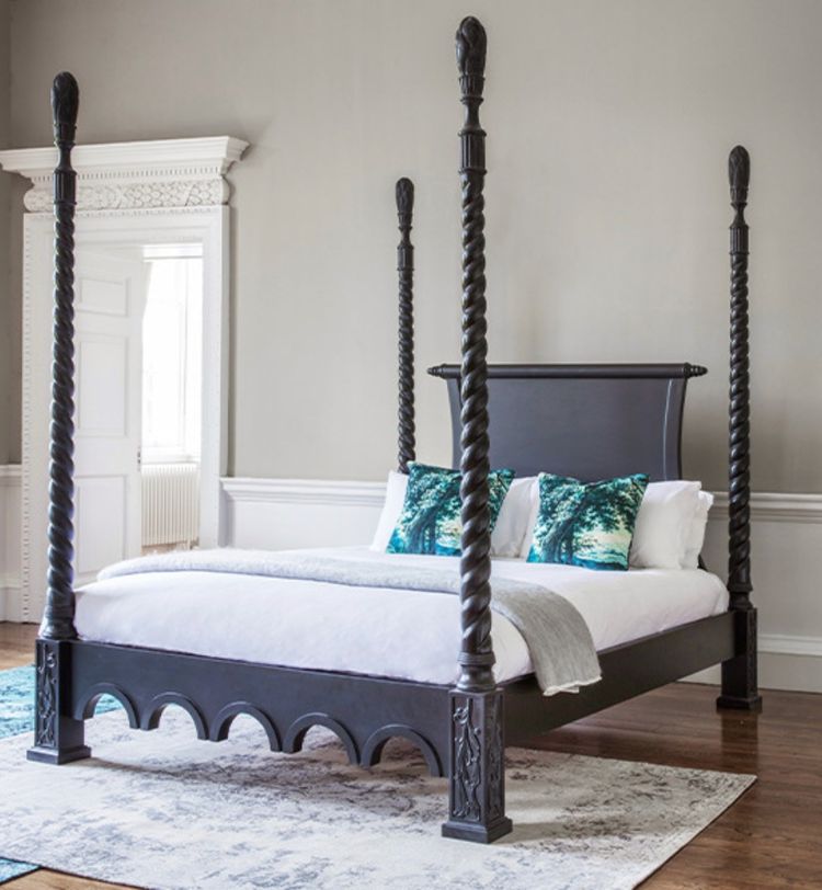 Elegant four-poster bed with twisted black columns, white bedding, teal pillows, and a light gray throw in a classic room with wooden floors.