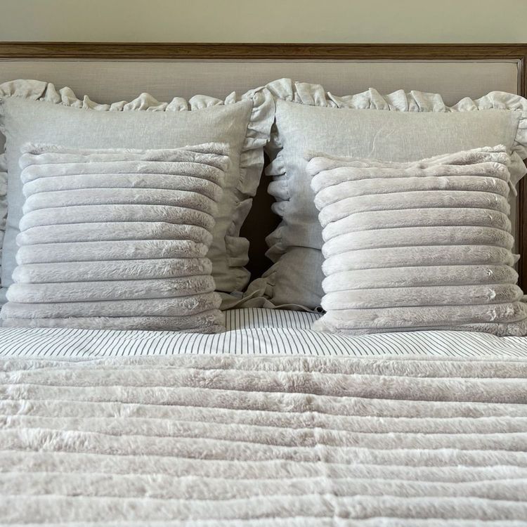 A neatly made bed with ruffled pillows and textured cushions, featuring a striped and plush comforter.