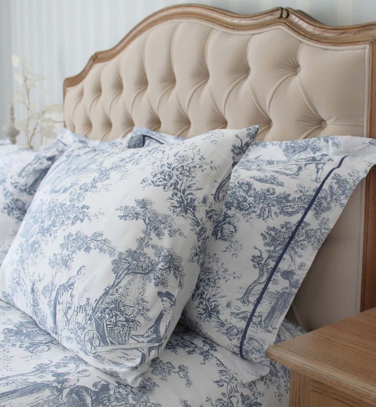 Elegant bed with tufted headboard, featuring blue and white toile-patterned bedding, next to a wooden nightstand.