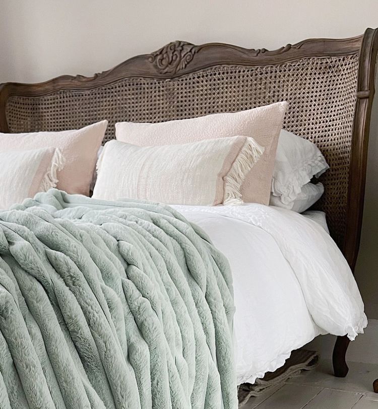 Elegant bed with a carved wooden headboard, white bedding, plush mint green throw, and decorative pillows in a cozy, softly lit room.