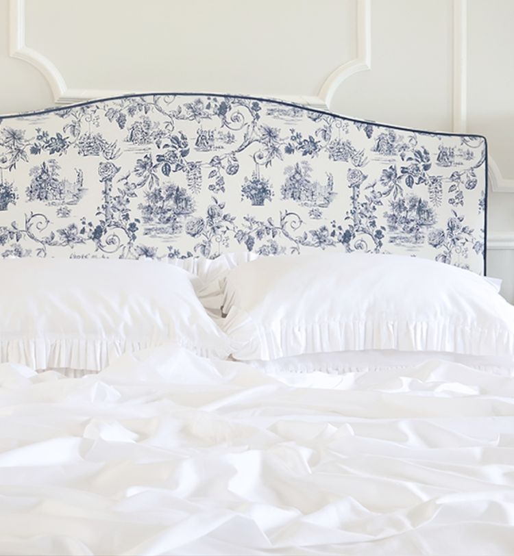 White bed with ruffled pillows and a detailed blue and white patterned headboard against a light wall with molding.