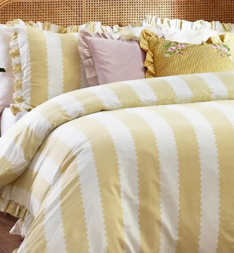 A bed with a yellow and white striped comforter, matching pillows, and decorative cushions, including a pink and an embroidered floral one.