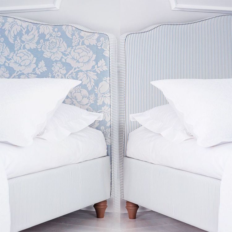 Two beds with white linens, one with a blue floral headboard and the other with a blue striped headboard, in a bright, minimalist room.