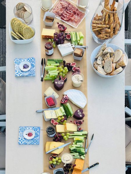 A table set with a variety of cheeses, meats, crackers, bread, fruits, and dips, arranged artfully for a charcuterie spread.